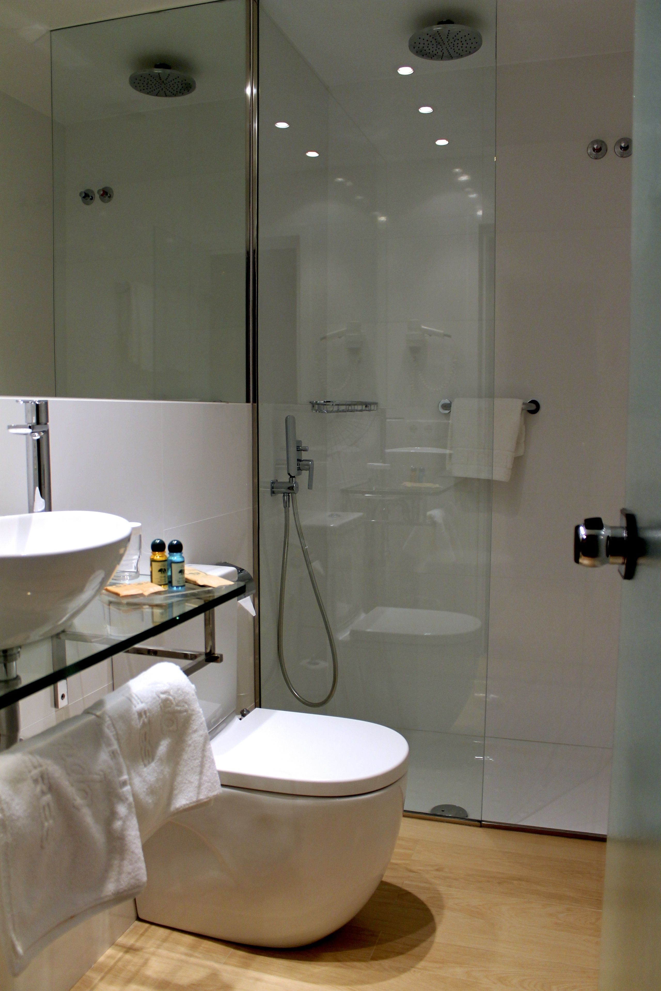 A modern bathroom with a glass-enclosed shower, a white toilet, and a glass sink with a mirror above it.