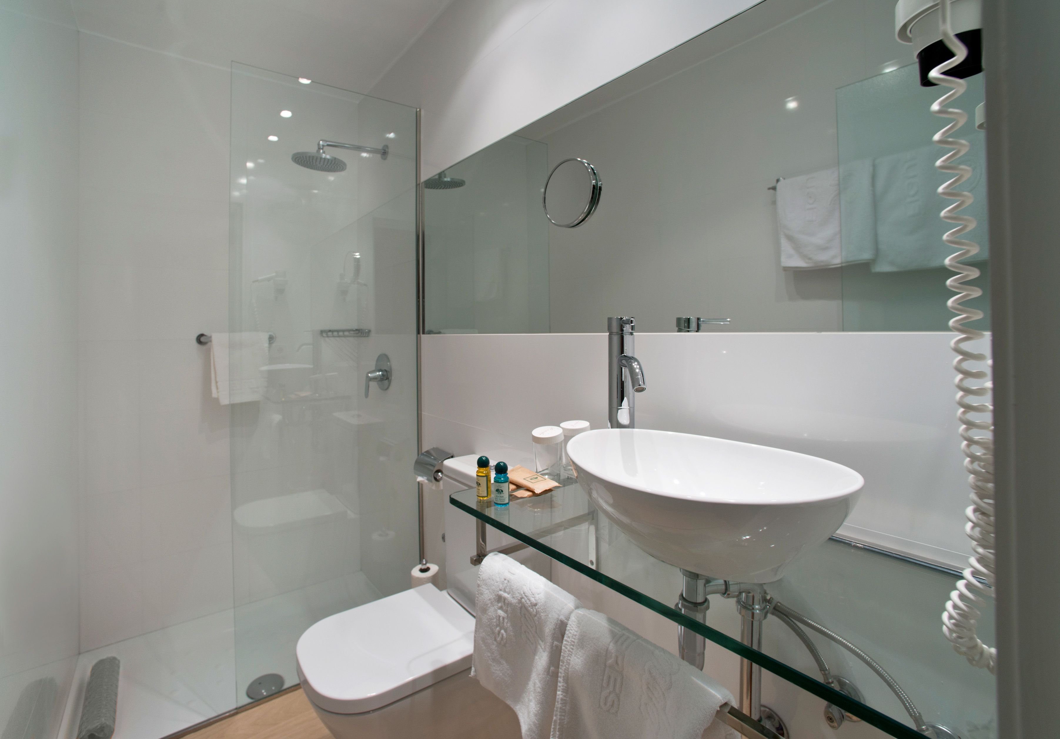 Un baño moderno con cabina de ducha de vidrio, lavamanos con cubierta de vidrio y tocador con superficie de vidrio.