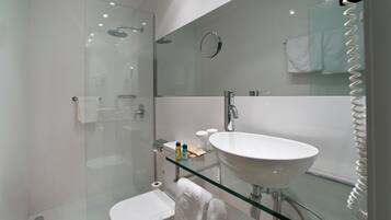 Un baño moderno con cabina de ducha de vidrio, lavamanos con cubierta de vidrio y tocador con superficie de vidrio.