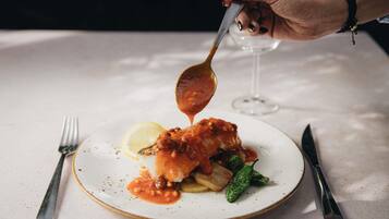 A plate of food with a spoonful of sauce being lifted, a fork, and a knife on the table.