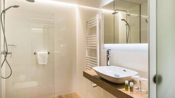 Een moderne badkamer met een douchecabine van glas, een witte wastafel en een houten opbergmeubel.