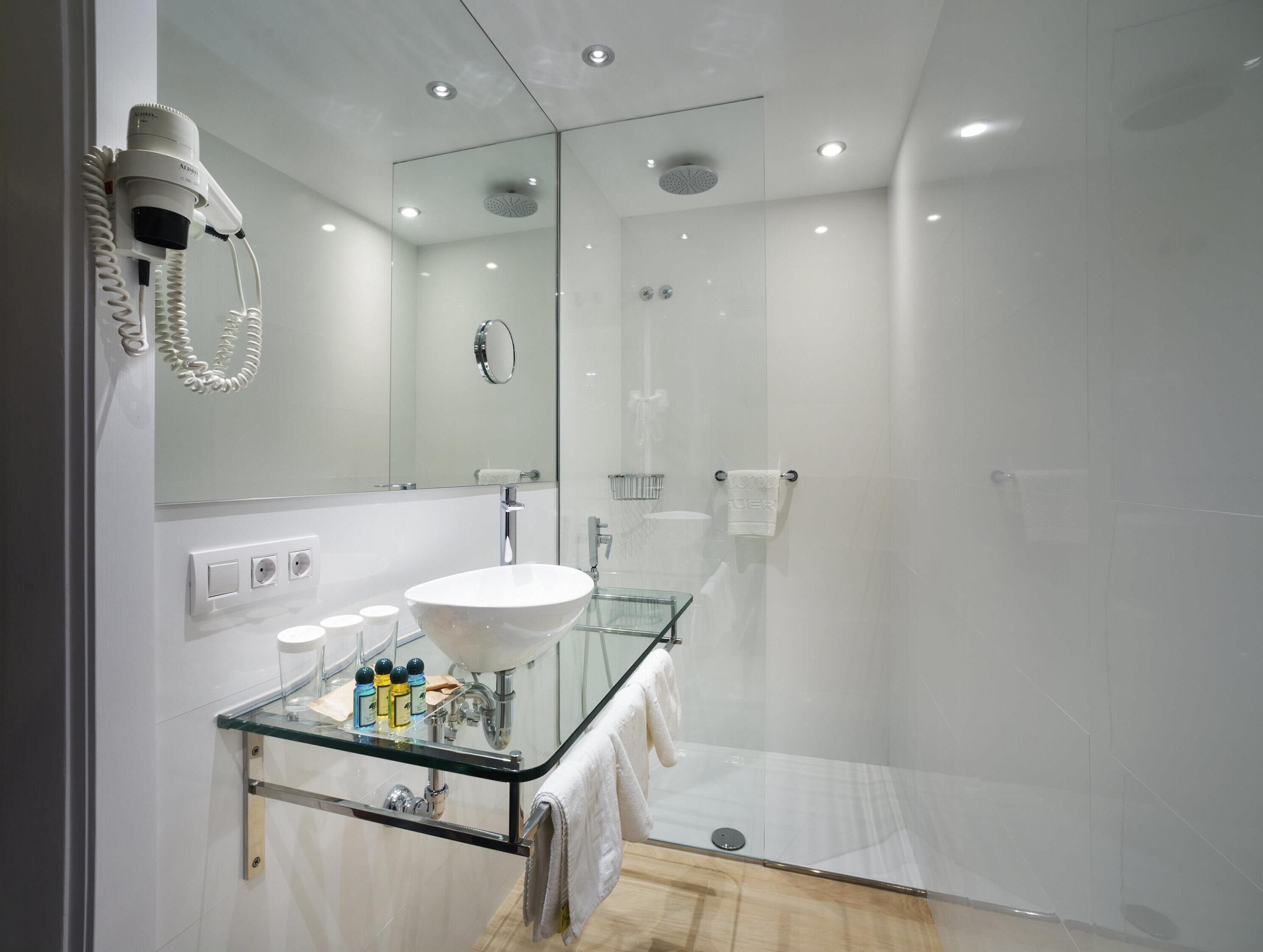 A modern bathroom with a glass-enclosed shower, a white sink, and a hairdryer mounted on the wall.