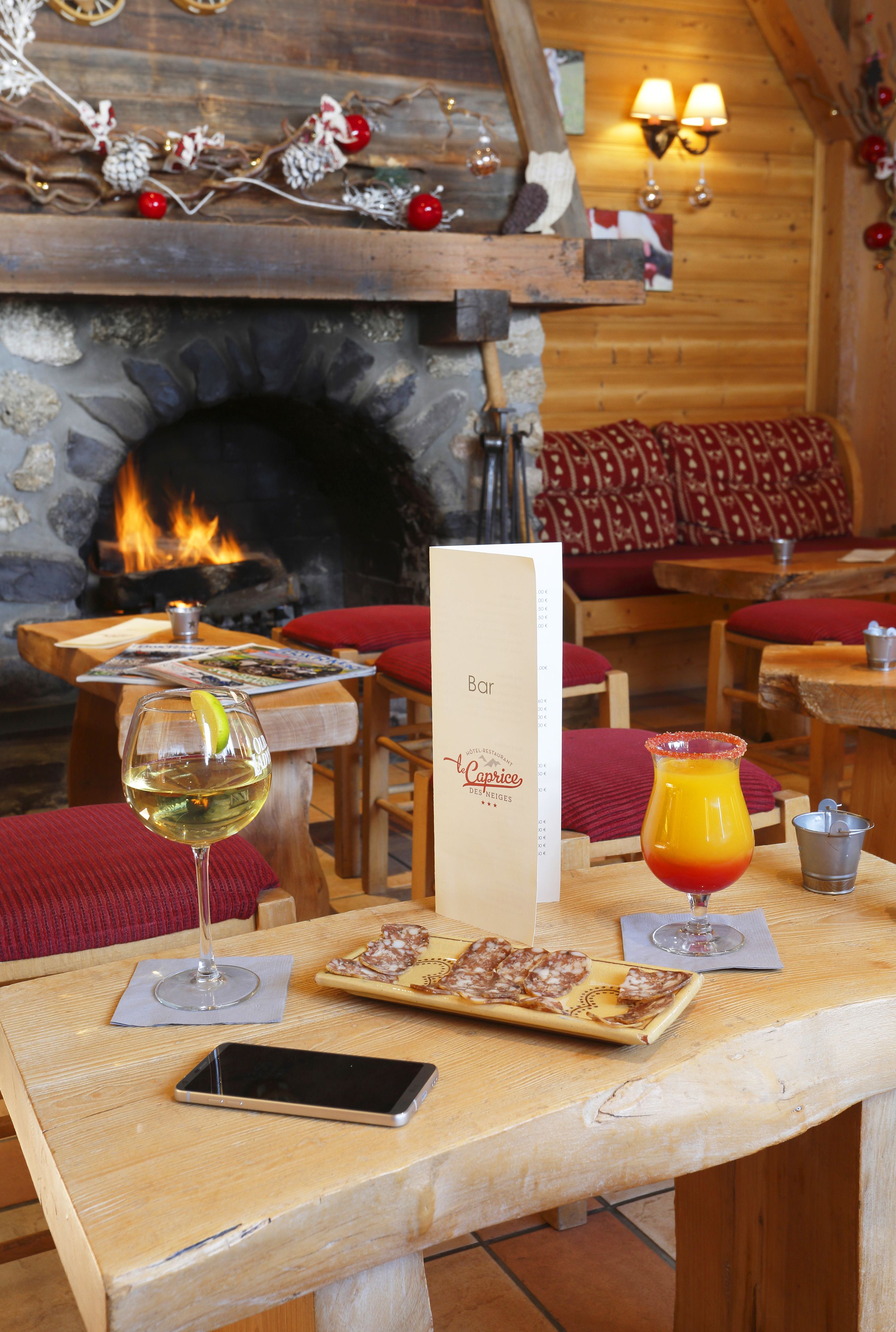 Une table en bois, un menu, un verre de vin blanc, un verre de jus d’orange et un téléphone intelligent.