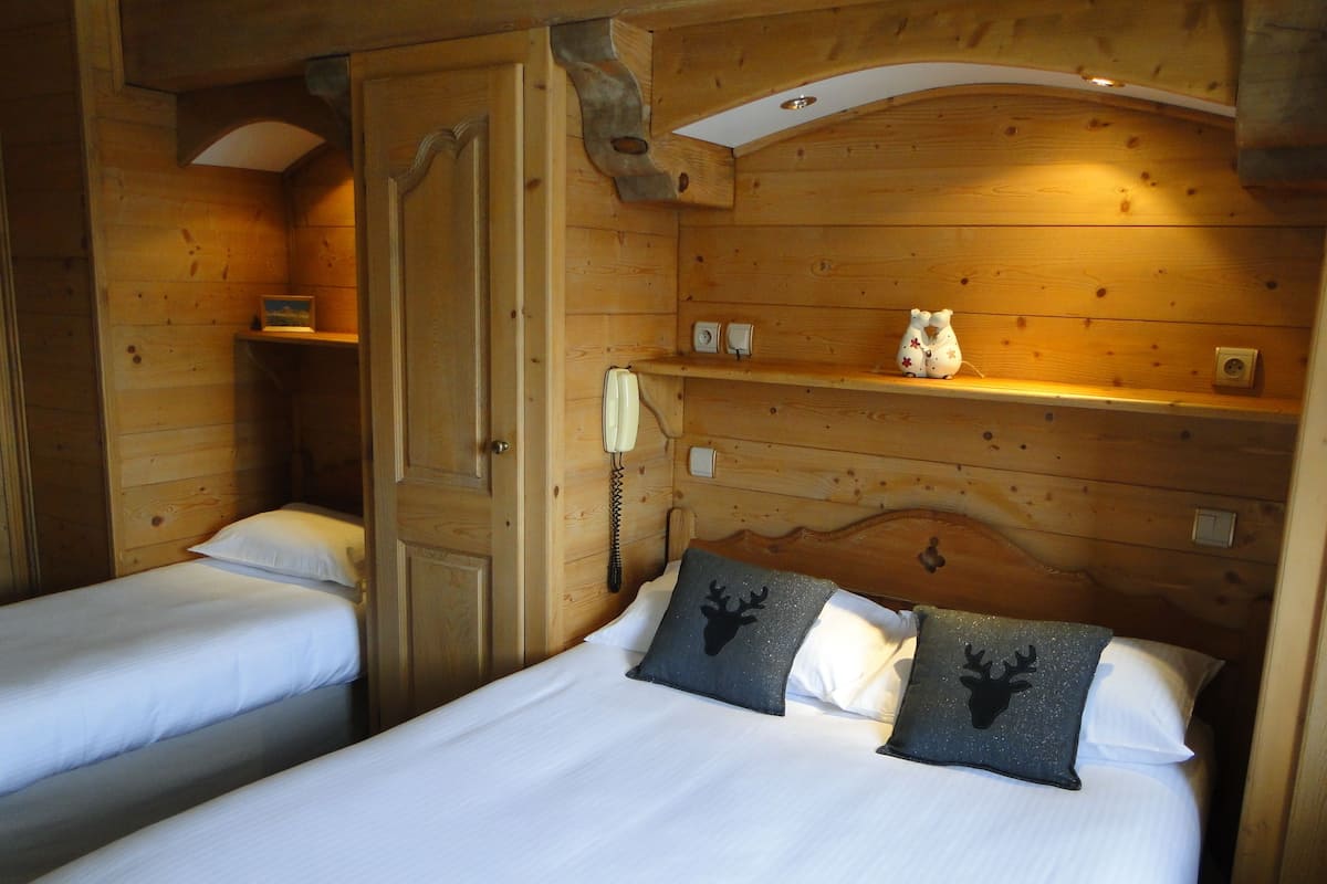 Une chambre dans un chalet en bois, avec deux lits, une porte en bois, une étagère avec un téléphone et une petite table avec une lampe.