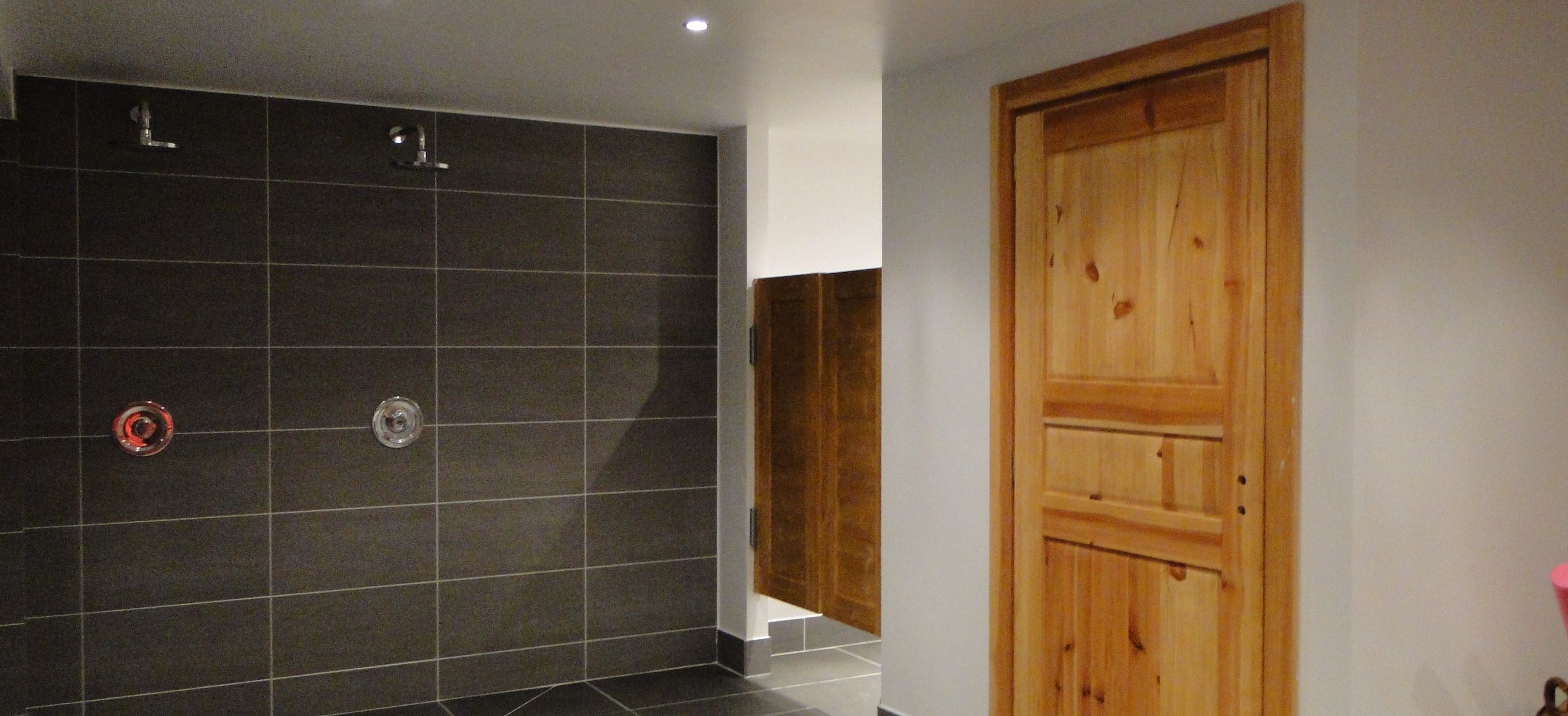 Un baño con paredes de baldosas oscuras, una puerta de madera y una zona de ducha.