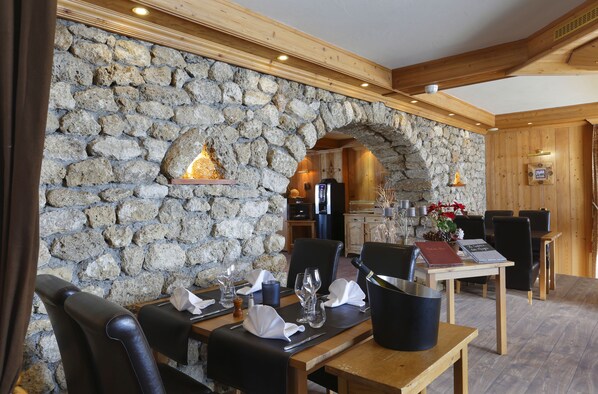 Un restaurante con paredes de piedra, vigas de madera y un arco de piedra. Las mesas están preparadas con copas de vino, platos y cubiertos.