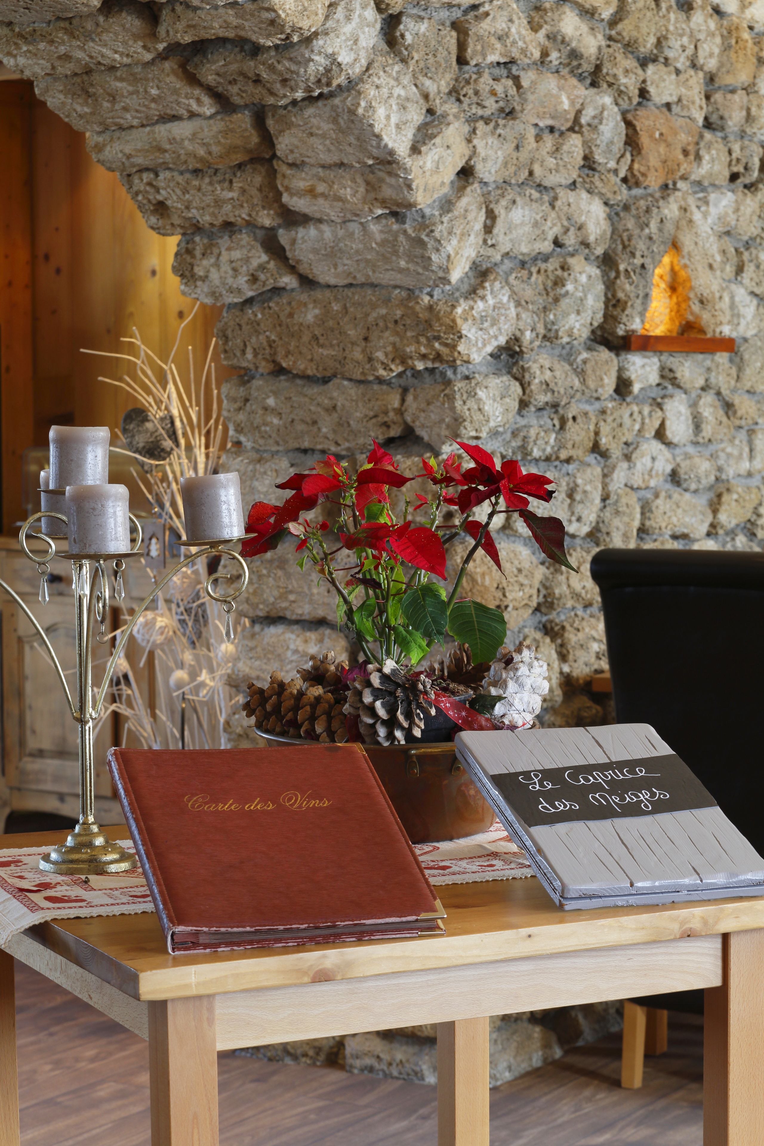 Una mesa de madera con un libro encuadernado en cuero, velas y una planta en maceta con flores rojas.