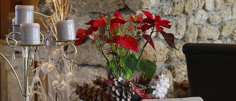 Una mesa de madera con un libro encuadernado en cuero, velas y una planta en maceta con flores rojas.