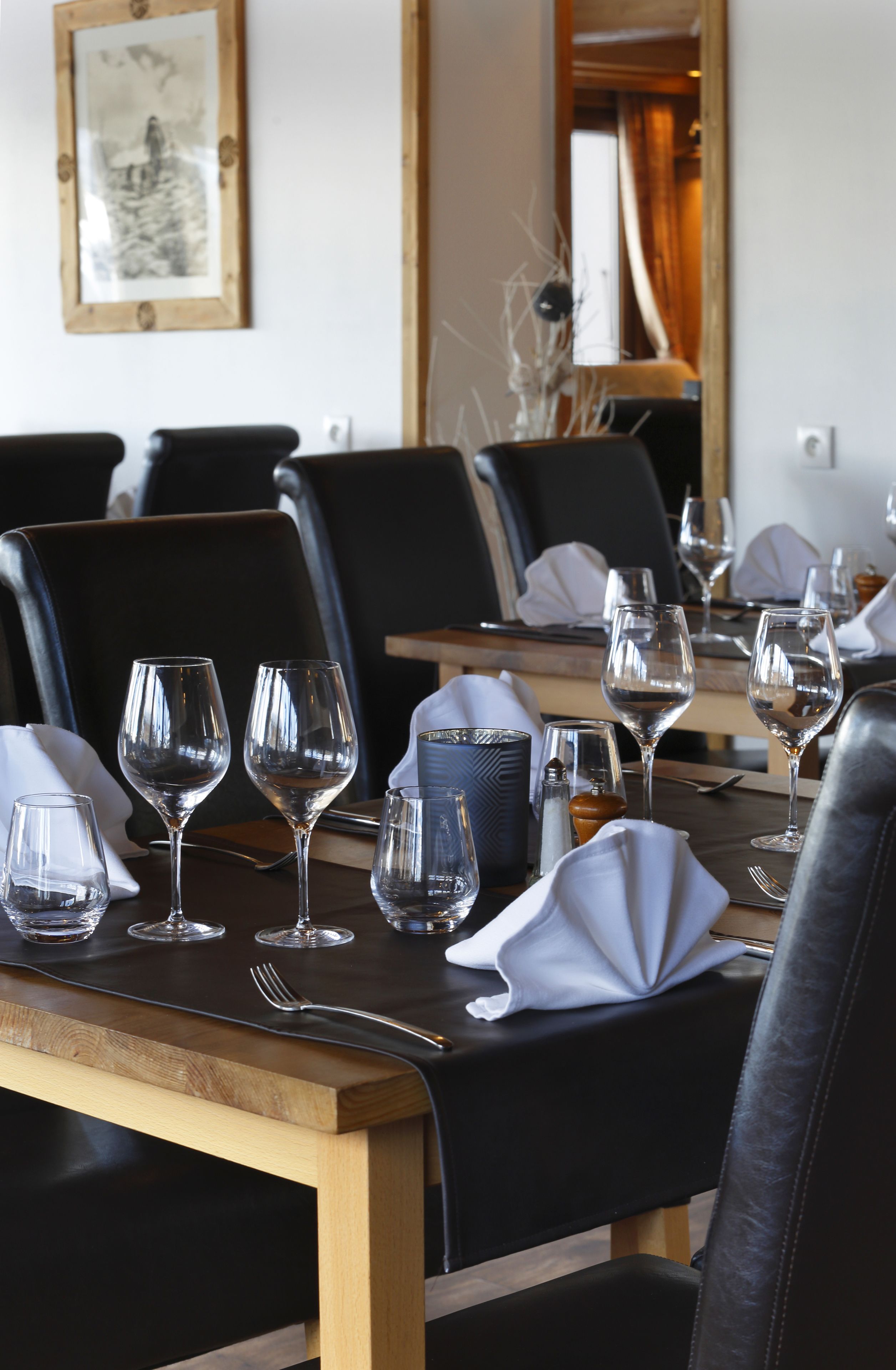 A dining area with tables set for a meal, featuring black leather chairs and wooden tables.