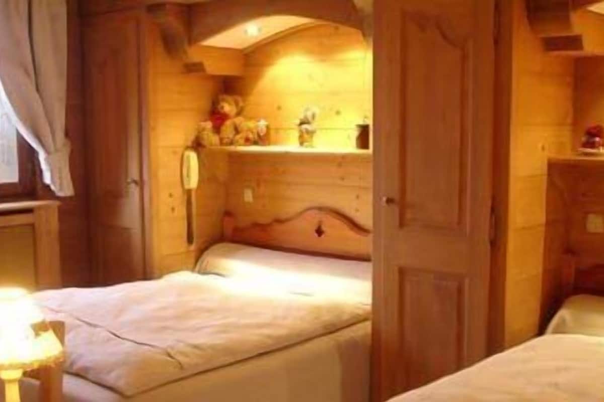 Une pièce chaleureuse en bois, avec deux lits, une petite table avec une lampe et une étagère où sont posés des objets personnels.