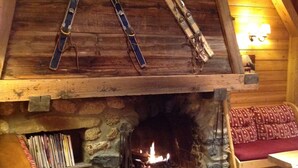 Interior acogedor de una cabaña de madera con chimenea de piedra, bancos de madera y esquíes colgados del techo.