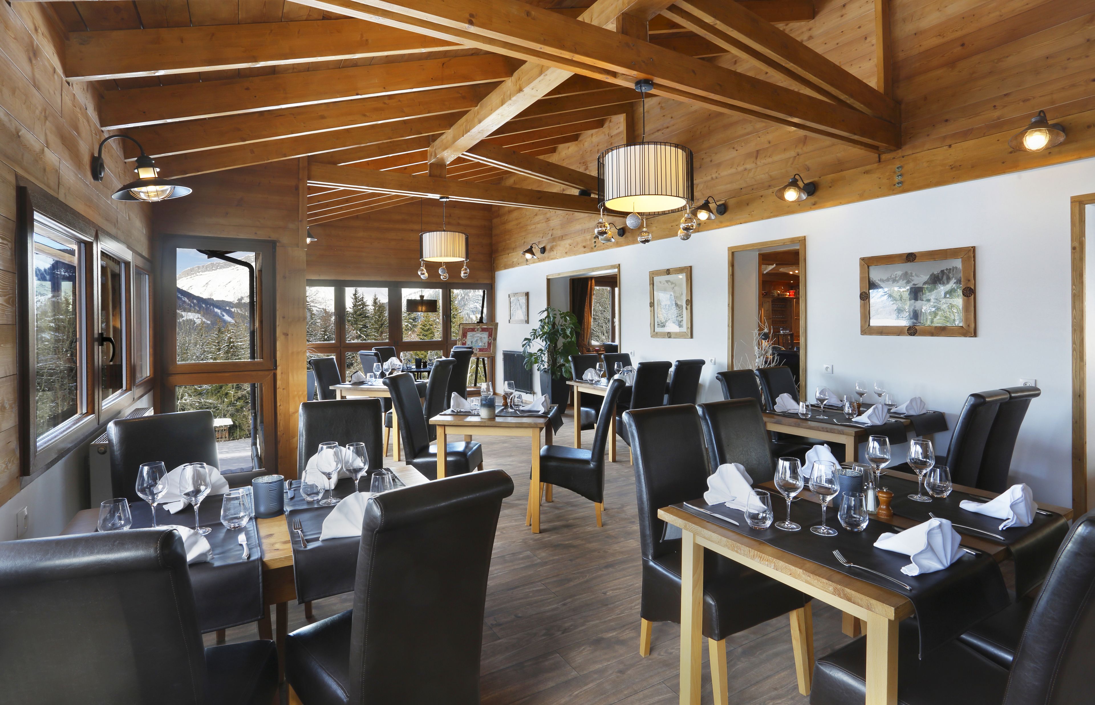 Een restaurant met houten balken en grote ramen met uitzicht op de bergen. Tafels zijn gedekt met wijnglazen en servetten.