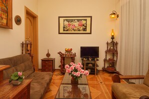 Sala de estar com sofá, mesa de centro com um vaso de flores, televisão e mesa lateral de madeira.