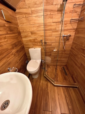 Une salle de bain avec un plancher en bois, des toilettes blanches et une douche séparée par des parois en verre.