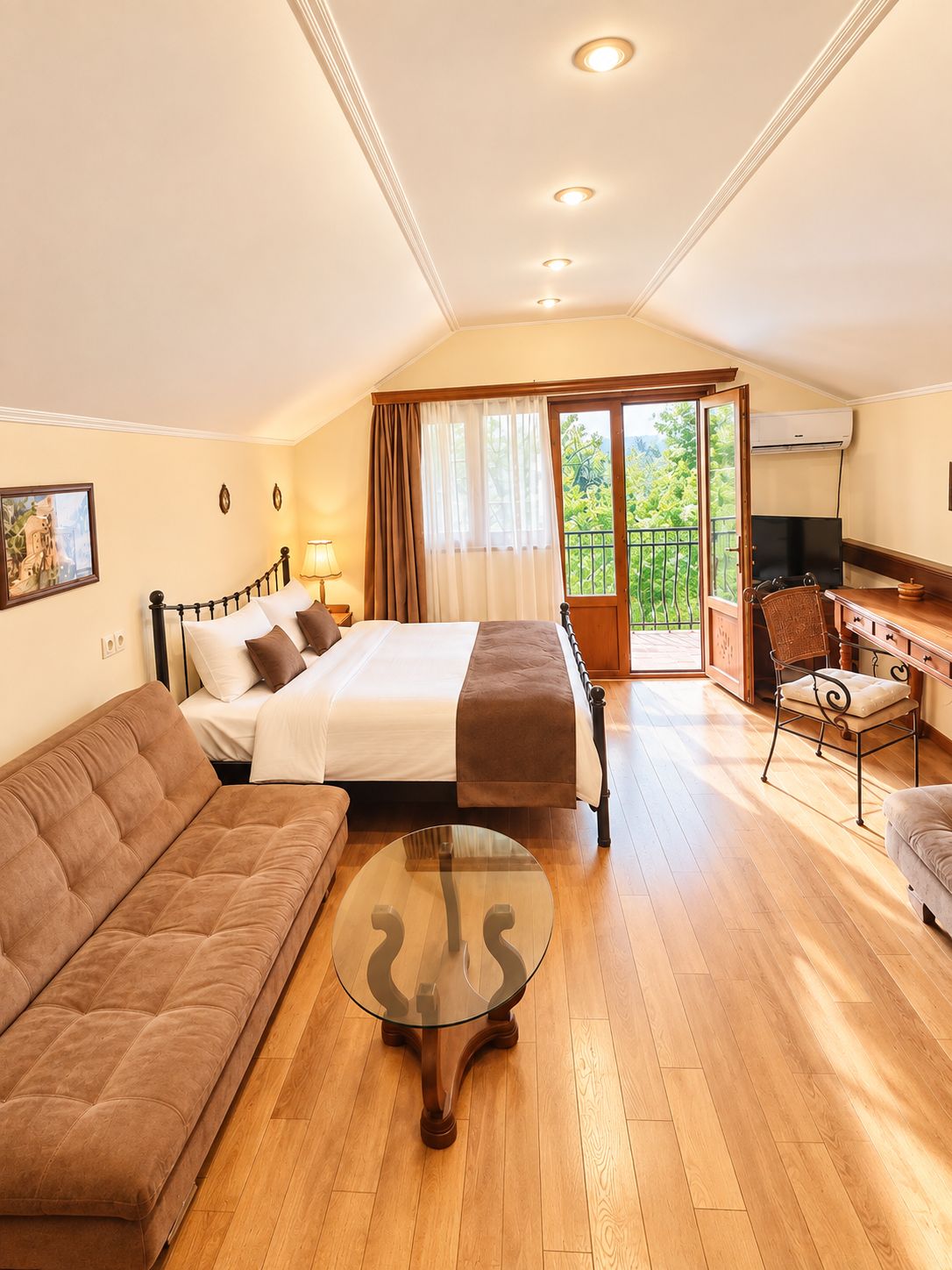 A hotel room with a bed, a sofa, a desk with a chair, a television, and a balcony with a view.