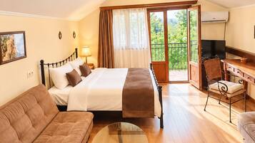A hotel room with a bed, a sofa, a desk with a chair, a television, and a balcony with a view.