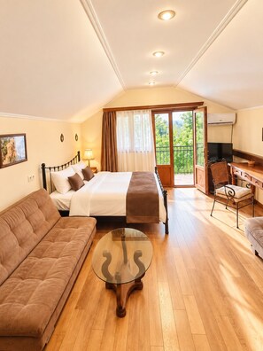 Habitación de hotel con cama, sofá, escritorio con silla, televisión y balcón con vistas.