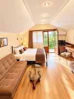 Habitación de hotel con cama, sofá, escritorio con silla, televisión y balcón con vistas.