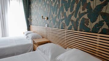 Camera d'albergo con due letti, una testiera in legno, un piccolo tavolino e una parete decorata.