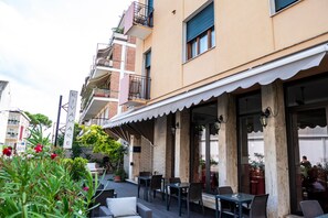 An outdoor café with tables and chairs, a building with a balcony, and a sign that reads "RIVAMARE".