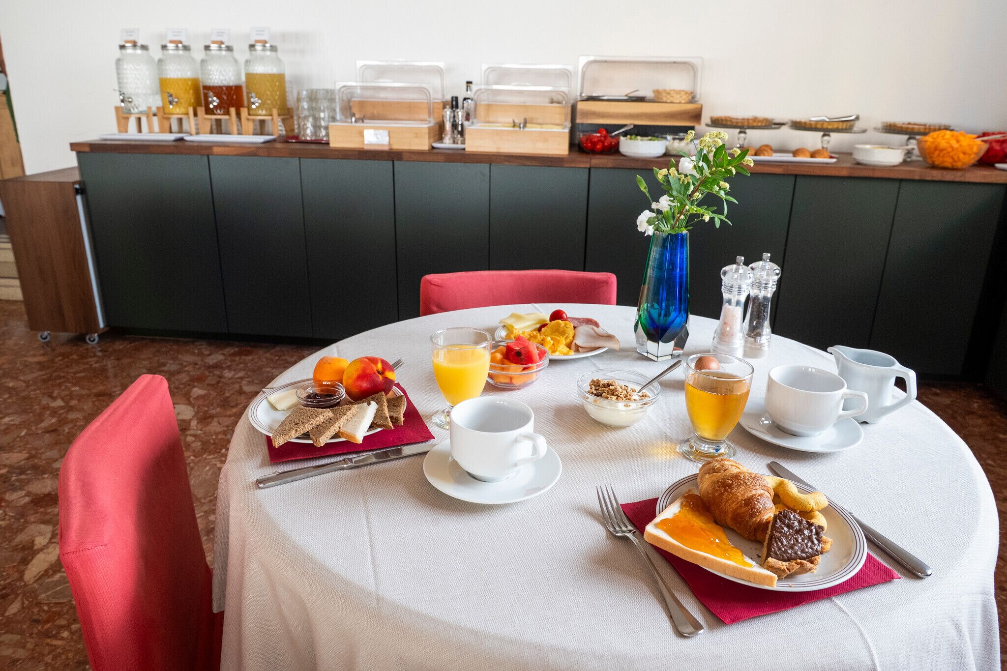 A breakfast setting with a table set for two, including plates of food, drinks, and a vase of flowers.