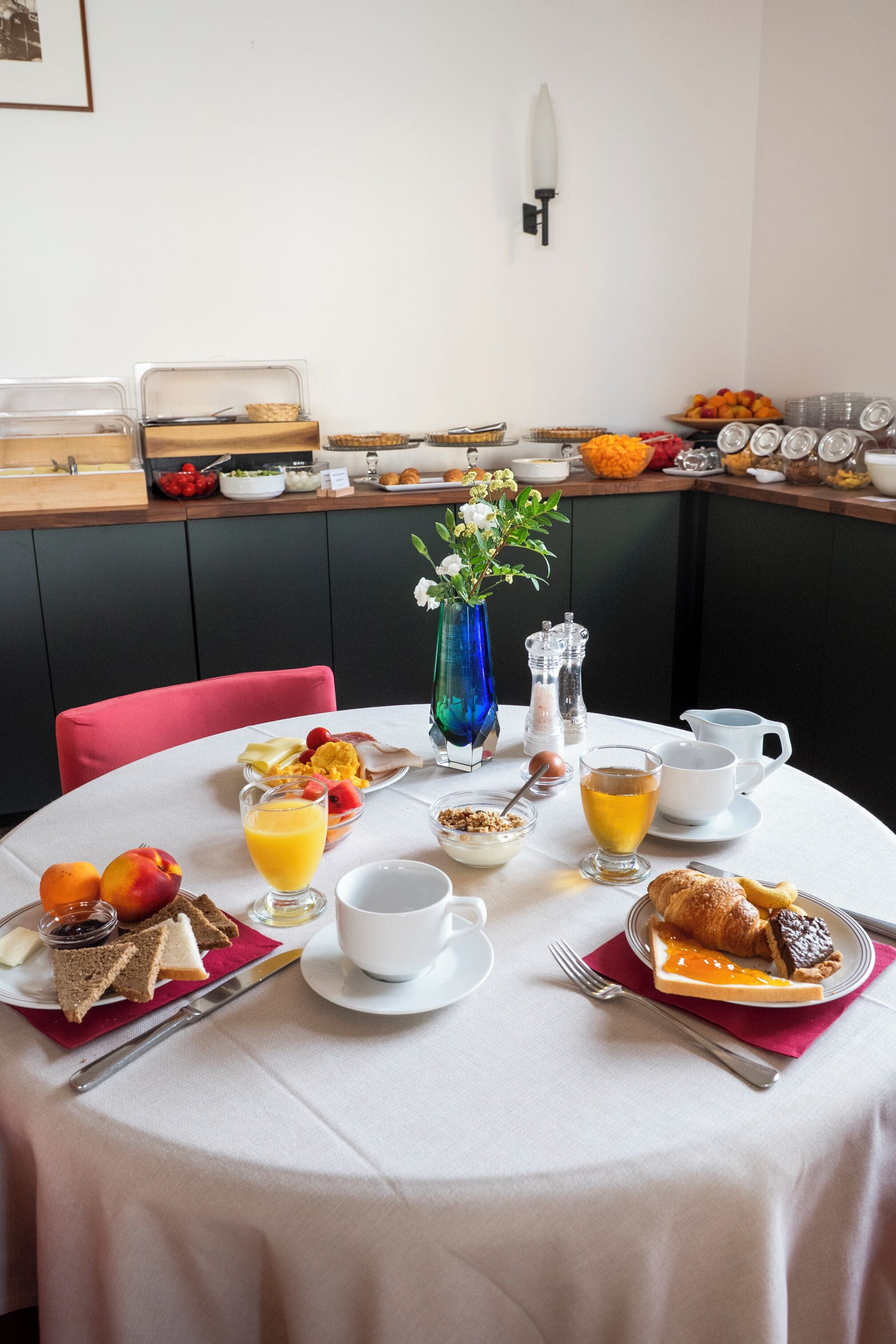 Ein Frühstückstisch reichhaltig gedeckt mit verschiedenen Speisen, darunter Obst, Gebäck und Getränke, in einem hellen Raum mit modernem Design.