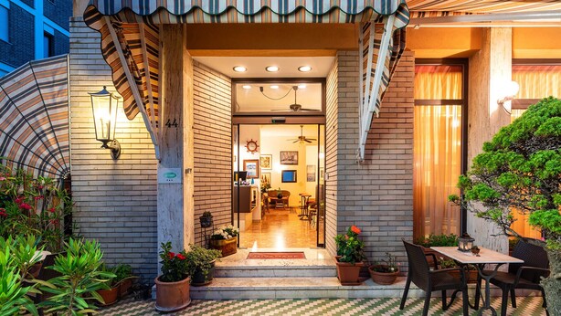 Entrada de hotel con fachada de ladrillo, un patio adoquinado y una zona de estar con mesas y sillas.