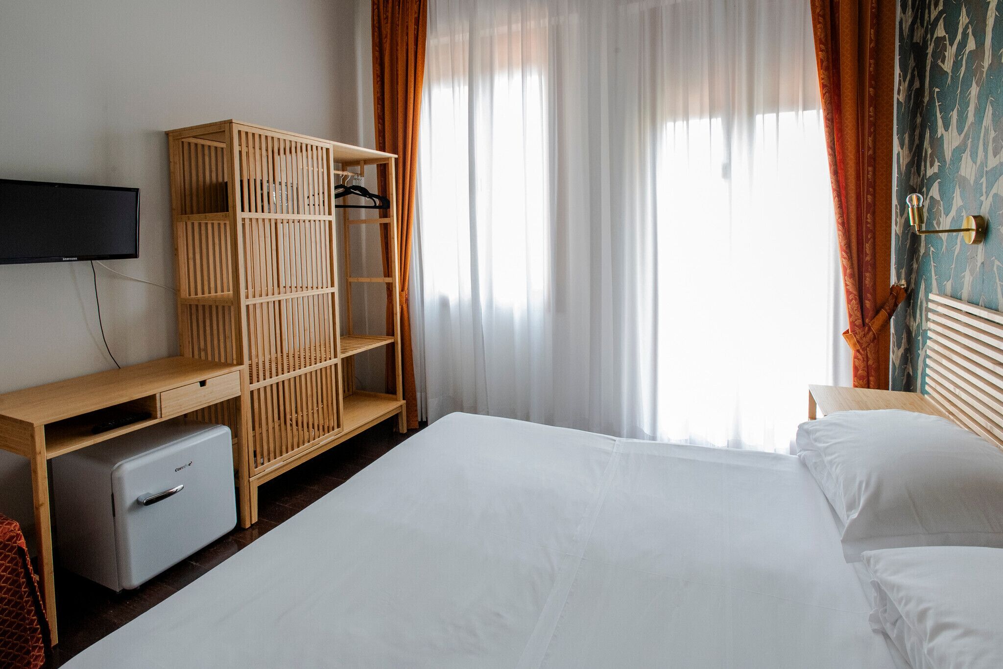 A bedroom with a bed, a wooden wardrobe, a desk with a computer, and a television.