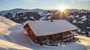 A wooden cabin with a snow-covered roof, surrounded by snow-covered mountains and a clear sky. - Hotel Elisabeth (Kirchberg in Tirol)