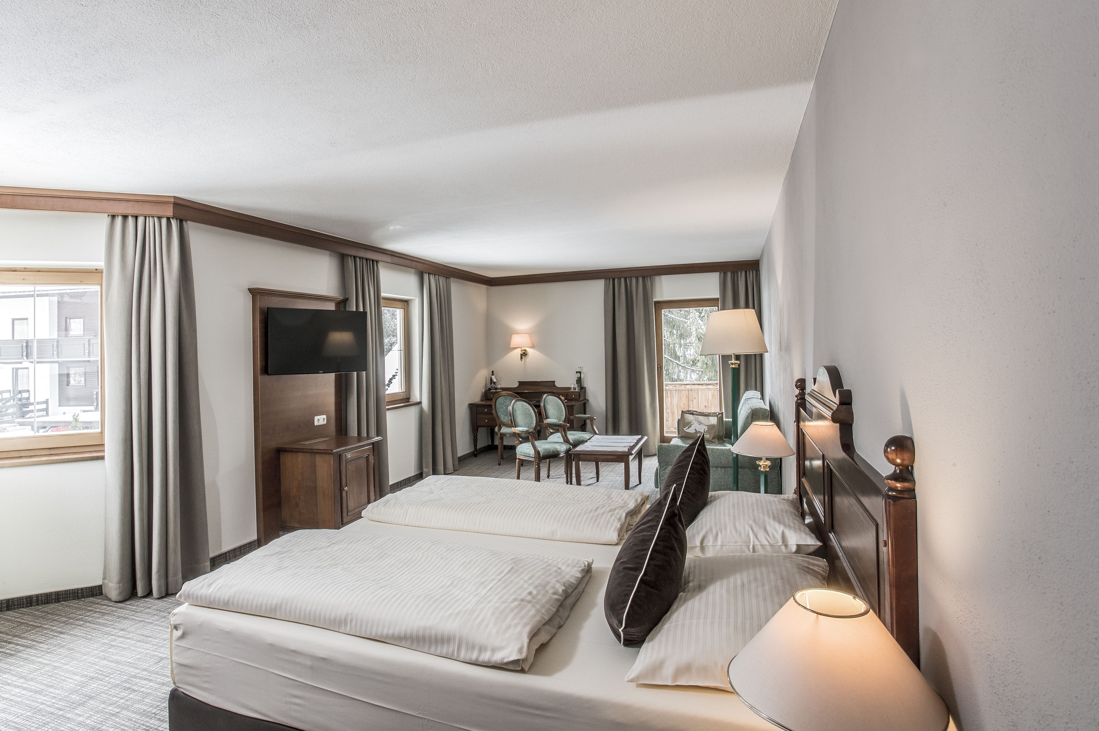 A hotel room with two beds, a desk, chairs, a TV, and a window with curtains.