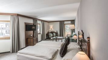 A hotel room with two beds, a desk, chairs, a TV, and a window with curtains.