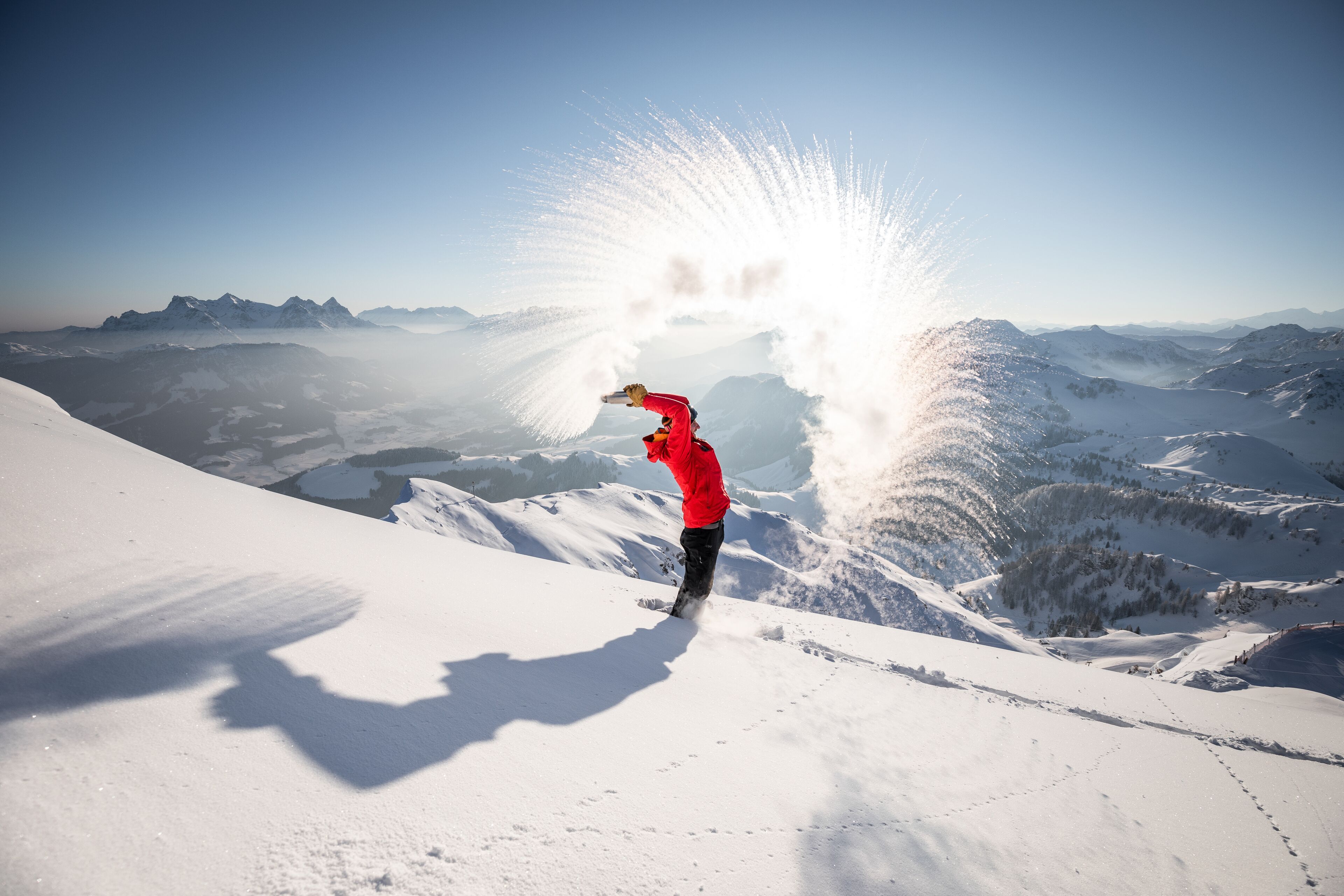 A person in a red jacket standing on a snowy mountain with a clear sky.
