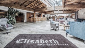 A spacious interior with high ceilings and wooden beams, featuring a bar area, seating, and a large potted plant. - Hotel Elisabeth (Kirchberg in Tirol)