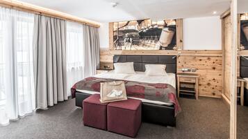Een hotelkamer met een bed, een houten hoofdbord, een nachtkastje, een bureau en een groot raam met gordijnen.