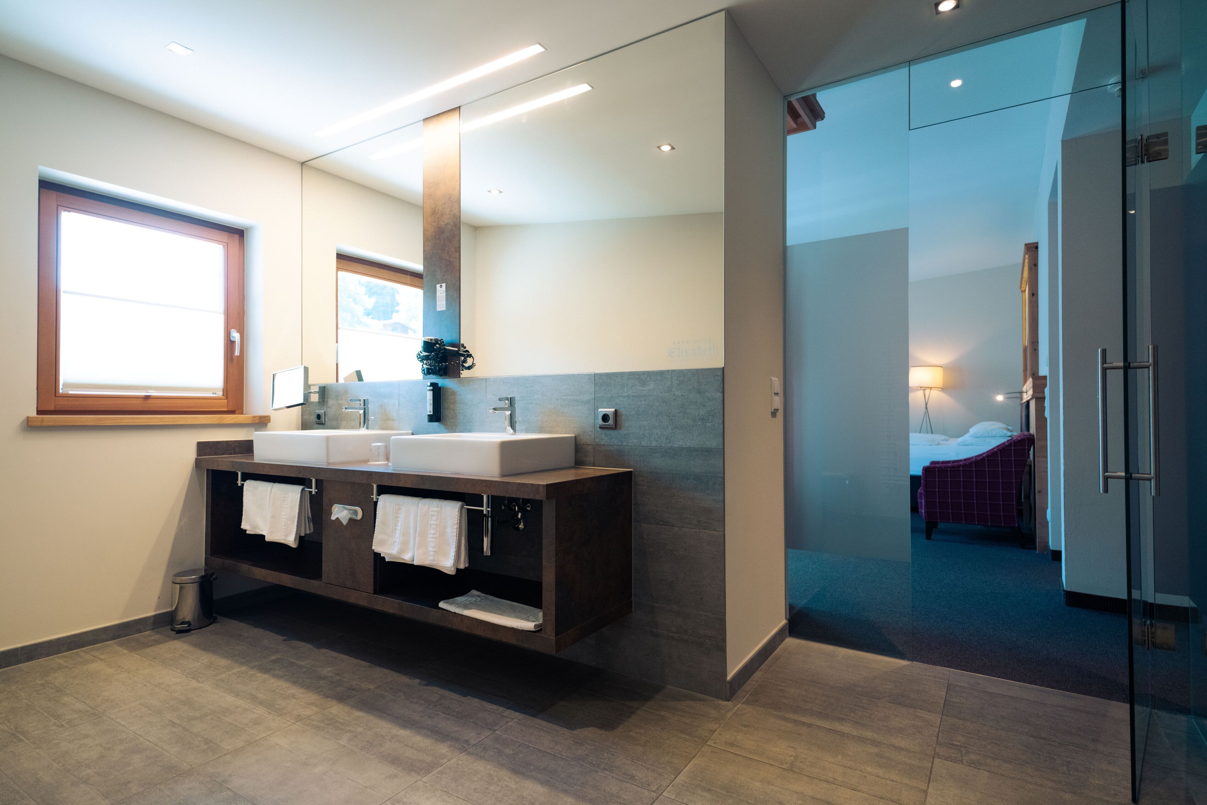 Une salle de bain moderne avec un meuble-lavabo à deux vasques, un grand miroir et une douche à parois de verre.