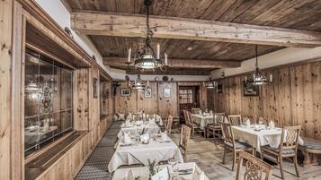 Un restaurante con paredes y techo de madera, mesas dispuestas con manteles blancos y candelabros.