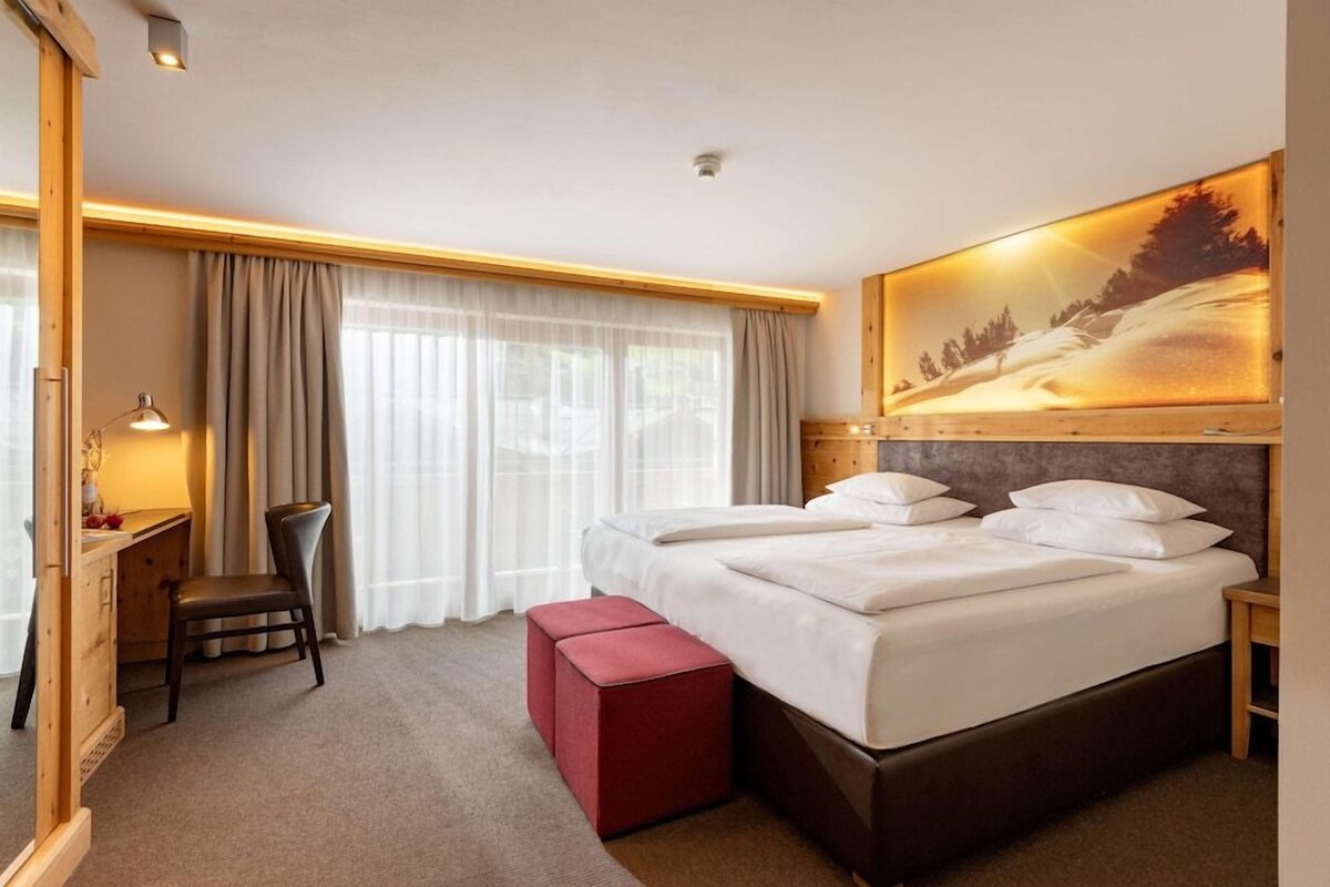 Habitación de hotel con una cama grande, un escritorio, una silla y un cuadro de un paisaje nevado.