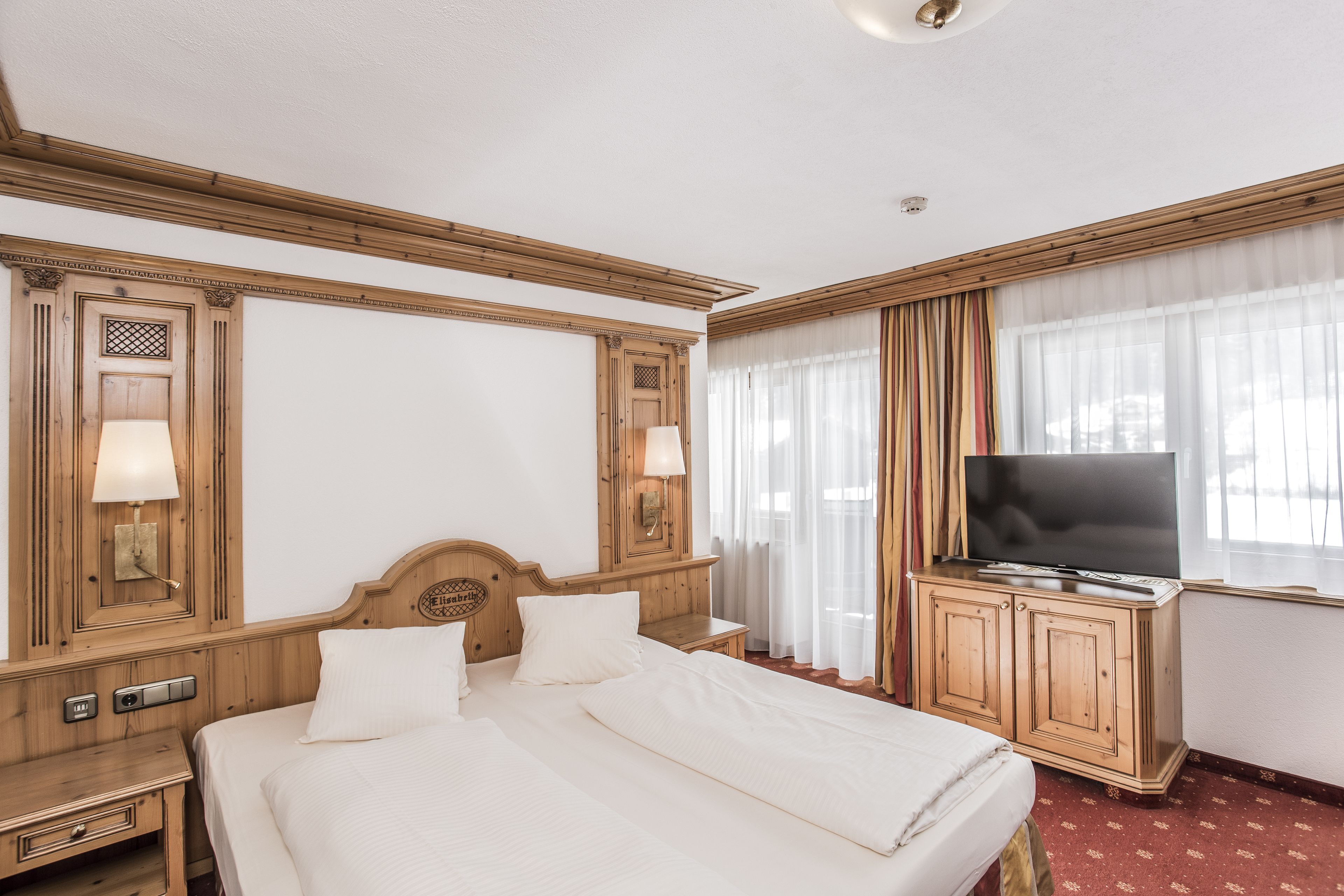 Une chambre d’hôtel avec un grand lit, un téléviseur posé sur un meuble en bois et une fenêtre avec des rideaux.