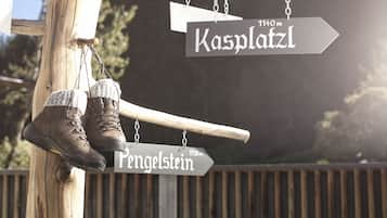 Un cartel de madera con indicaciones direccionales hacia 'Kasplatz' y 'Pengelstein', mostrando distancias de 1140m y 1938m respectivamente. Un par de botas cuelga del cartel.