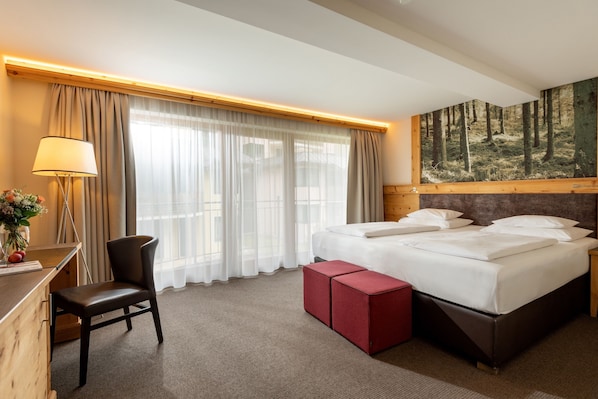Habitación de hotel con cama, escritorio con lámpara, silla, reposapiés rojo y un mural temático de bosque.