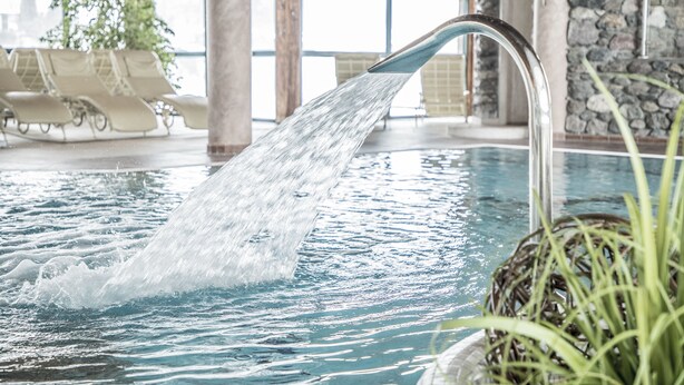 A pool with a water feature, lounge chairs, and a stone wall. - Hotel Elisabeth (Kirchberg in Tirol)