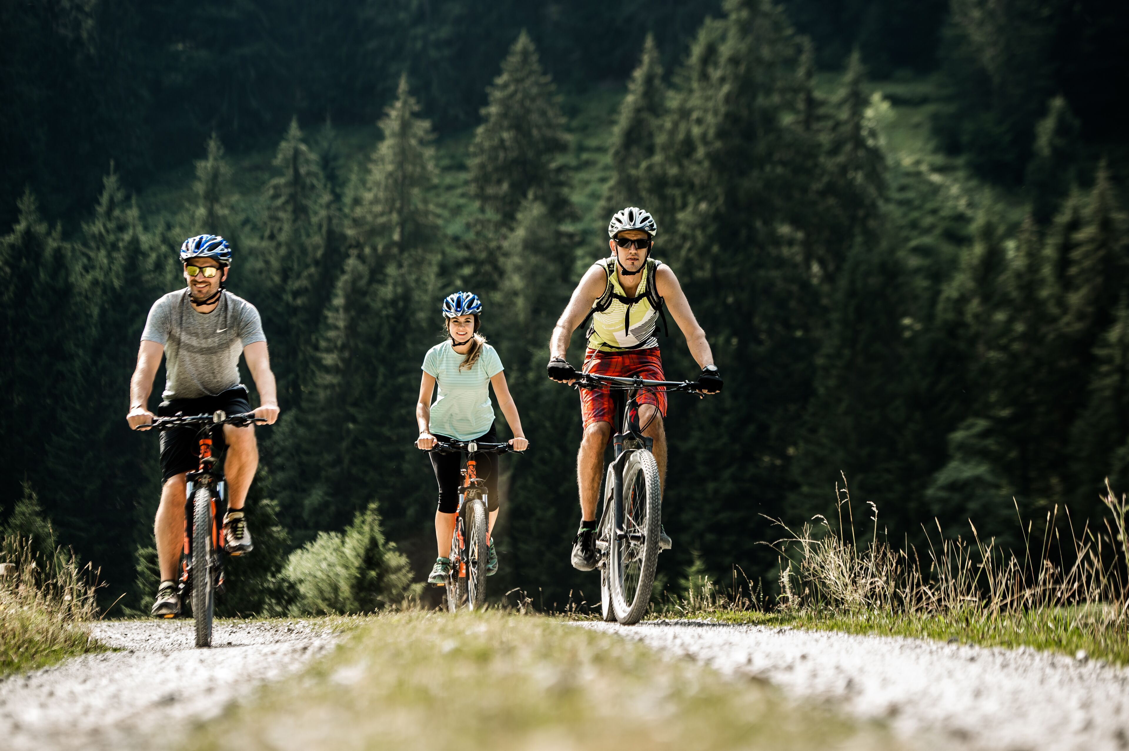 Tre ciclisti su un sentiero sterrato immersi in una fitta foresta.