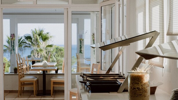 A dining area with a view of the ocean, a buffet setup with plates and serving utensils, and a ceiling fan.
