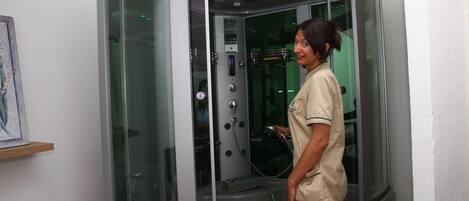 A glass-enclosed, modern shower stall with a control panel and a handheld showerhead.