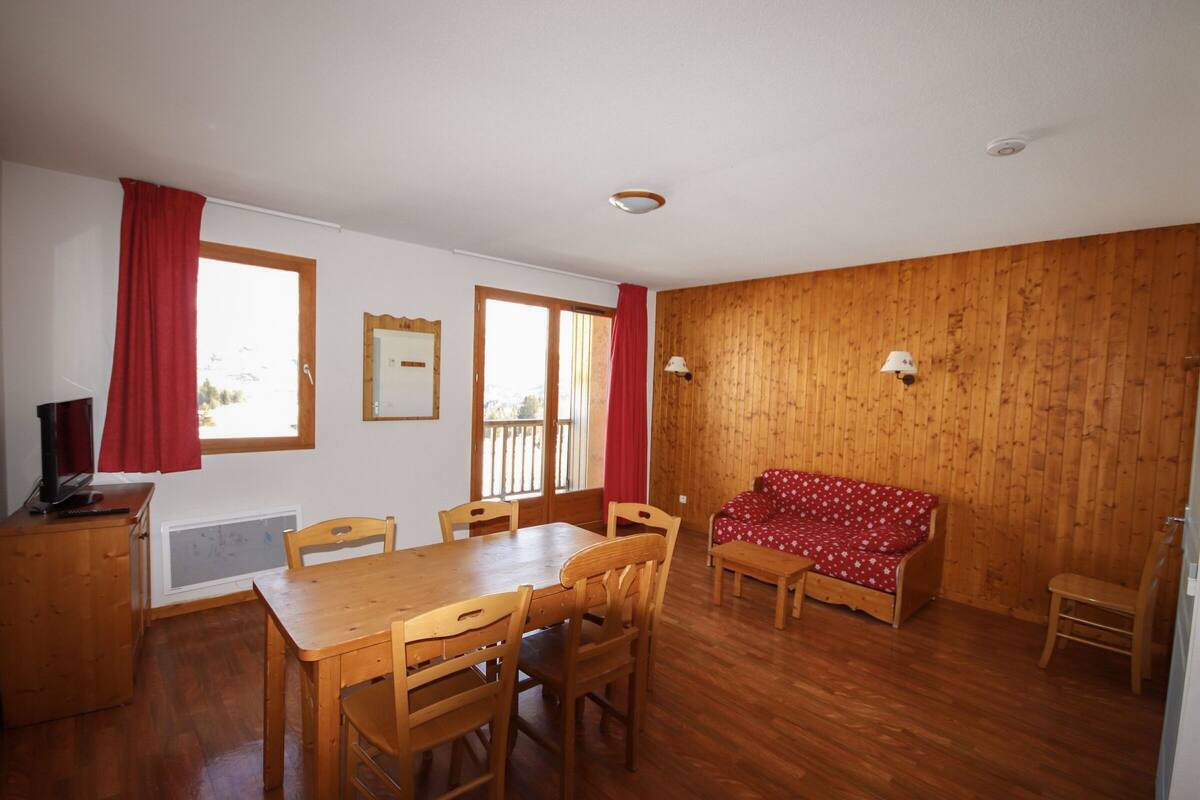 Ein Zimmer mit einem Holzesstisch, Stühlen, einer Couch und einem roten Vorhang.