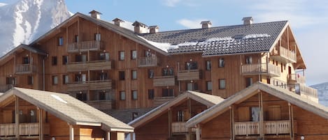 A wooden chalet-style hotel with multiple balconies and a mountain backdrop.