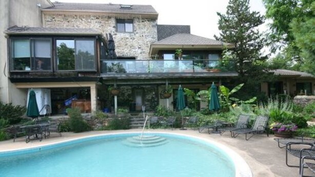 A swimming pool with lounge chairs and umbrellas, surrounded by a stone building with a balcony. - Alpenhof Bed and Breakfast (Media)