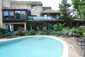 A swimming pool with lounge chairs and umbrellas, surrounded by a stone building with a balcony. - Alpenhof Bed and Breakfast (Media)