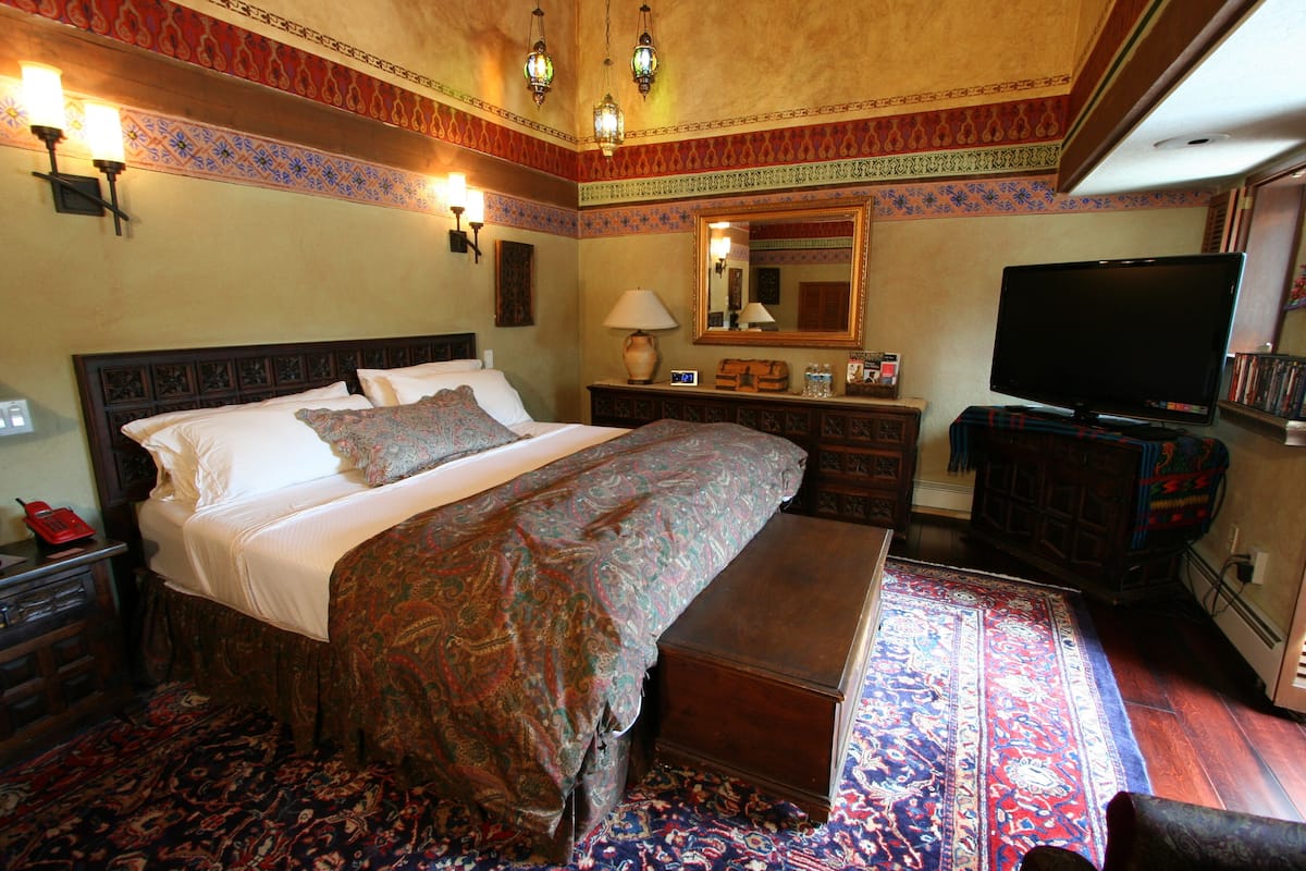Habitación de hotel con una cama grande, un banco, un televisor, una mesita de noche y un aparador.