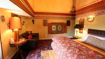 A room with a bed, a table with a lamp, a sofa, and a patterned rug.